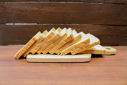 Fresh sliced bread arranged on a wooden cutting board over a rustic wooden table. Fresh delicious gourmet food background on the table rustic side view copy space.