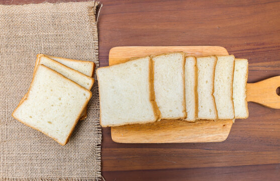 Fresh sliced ​​bread arranged on a wooden cutting board with one slice leaning against the stack over a rustic wooden table. top view copy space.
