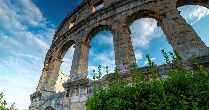 Time lapse of rushing clouds over the ancient Roman amphitheater of Pula Arena in Croatia with historic stone arches under a blue sky