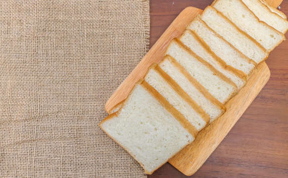 Fresh sliced ​​bread arranged on a wooden cutting board with one slice leaning against the stack over a rustic wooden table. top view copy space.