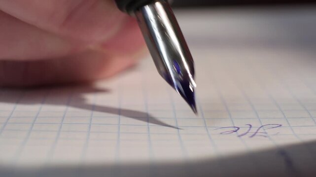 Hand with fountain pen with metal nib in ink writing letter on notebook sheet of paper close-up
