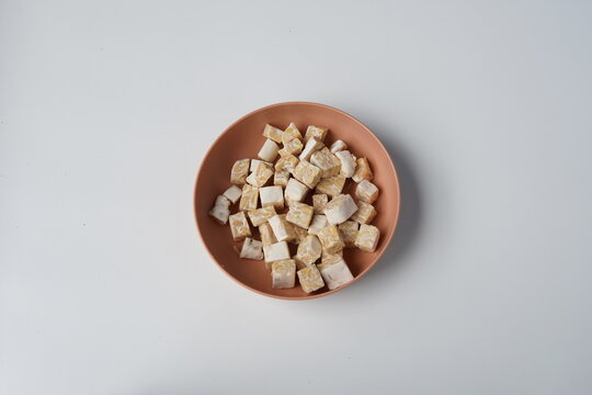 raw diced tempeh pieces on brown plate. cut tempe blocks. resh soybean tempeh cubes. tempeh food isolated background