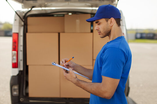 Logistic, shipping service. Delivery man with clipboard standing by car, checking list and distribution of orders, van full of cardboard boxes