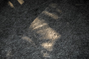 Fototapeta premium The surface of the fabric is dark gray with a rough and fibrous texture. Sunlight entering from the side creates contrasting warm highlights on the surface of the fabric