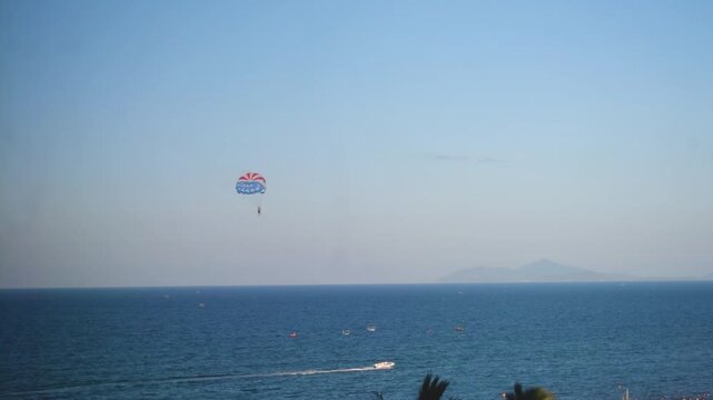 Colorful parasailing adventure over the sea with a speedboat towing the parachute against a clear blue sky. Popular coastal tourism activity offering thrill, happiness, safety, and scenic ocean views.