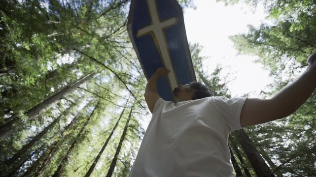 Man Lifting Blue Cross Sign Overhead in Redwood Forest - Low Angle