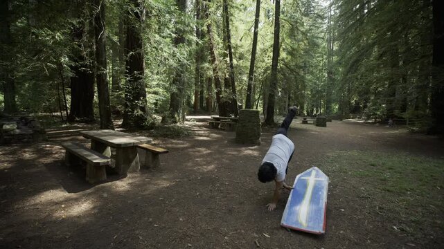 Man Doing Professional Tricks With Painted Board in Forest Picnic Area - Wide, Steady Cam Shot