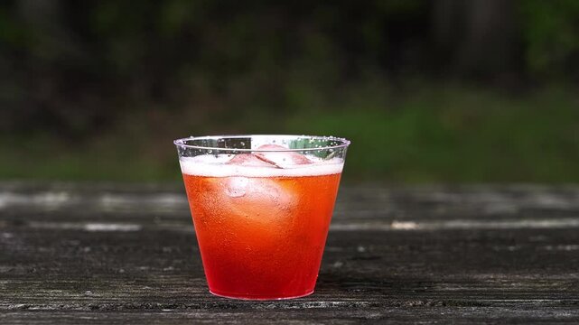 Refreshing spritz cocktail being prepared on a rustic wooden table. Person adds soda to red drink 