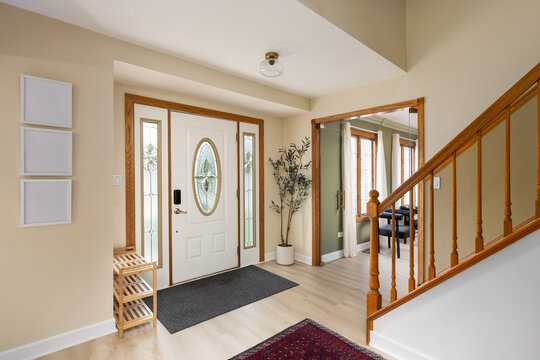 A home entryway with tan walls, wood floors and trim, a front door with decorative frosted glass, and looking towards a green living room.
