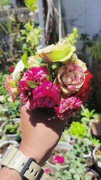 Hand holds colorful bouquet of roses and flowers in garden setting