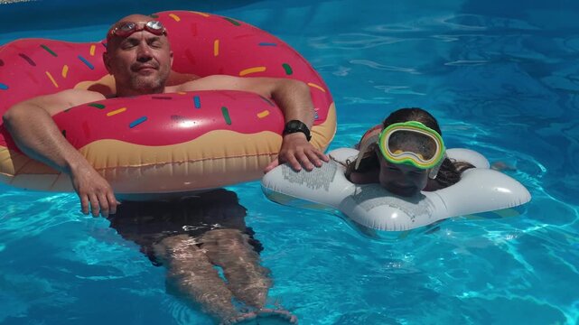 Happy smiling man in donut float and girl in diving mask swimming in pool. Concept of family summer vacation