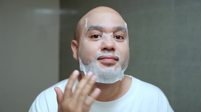 Man applying a sheet mask in front of a bathroom mirror during his morning skincare routine. Healthy aging longevity. Men self-care anti-aging skincare. wellness and preventive health concept.
