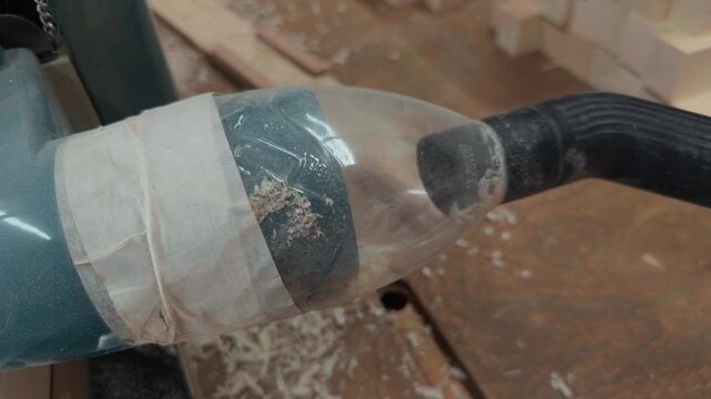 Authentic Macro Shot of Custom Dust Extraction Attachment on Industrial Woodworking Thickness Planer Machine with Sawdust and Wood Shavings Sucked Through Clear Adapter in Workshop Environment
