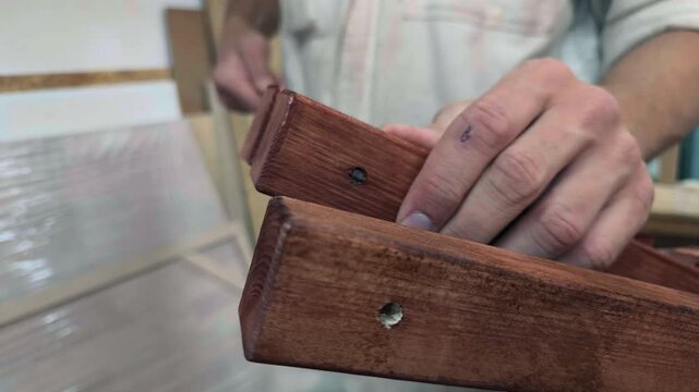 Extreme close up of an anonymous self-funded craftpreneur guiding a long steel threaded shaft through dark wooden ribs and circular dividers during outdoor furniture assembly in a bootstrap startup