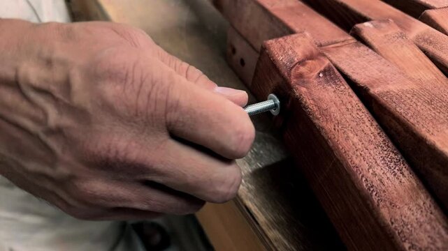 Extreme close up of unrecognizable male hands securing a metal acorn nut onto a threaded steel rod connecting wooden furniture components during authentic assembly inside a home based microbusiness