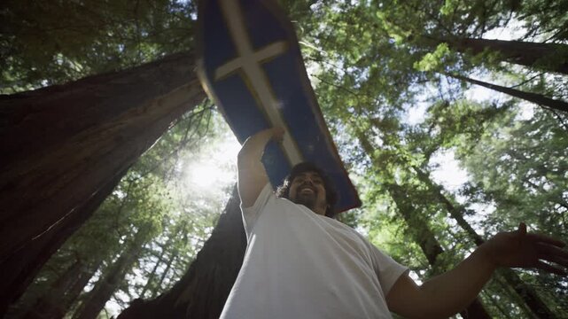 Man Holding Blue Cross Board Overhead in Redwood Forest Low Angle In Slow Motion
