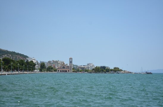 
Cityscape. A church and a city clock tower in the distance. Sea in the foreground. Volos, Greece, June 2026