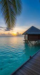 Fototapeta premium Overwater bungalow at sunset over turquoise ocean, framed by palm frond, symbolizing tropical vacation, serenity, and paradise