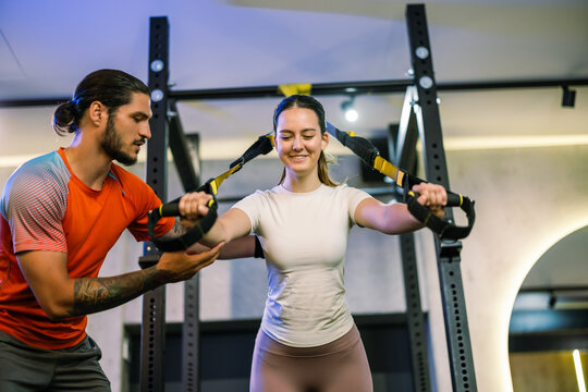 A personal trainer helping a woman perform a suspension strap chest exercise in the gym