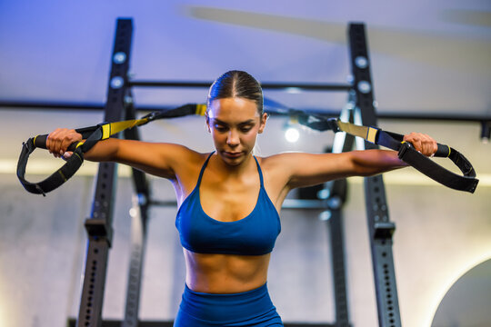 Fit female model maintaining perfect form during a suspension strap workout in a gym.