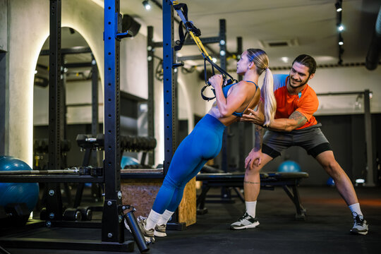 A personal trainer correcting a woman form during a suspension strap row exercise in the gym