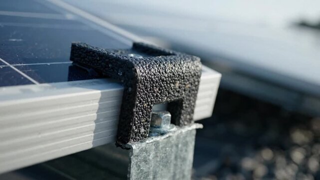 Macro shot of a textured black bracket securing solar panels on a rooftop under bright daylight.