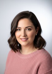 Fototapeta premium Studio portrait of an attractive smiling woman with wavy dark hair wearing a cozy pink knit sweater against a white backdrop