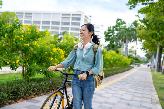 Young Asian female student riding a bicycle on her way to university along the bike lane