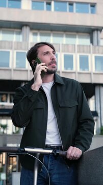 Young businessman talking on his smartphone while standing with an electric scooter
