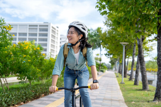 Relaxed, happy young Asian female with toothy smile riding a bike during in the city park on her way from work to home.