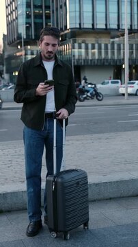 Man with suitcase standing on a city street waiting for his ride after booking it with an app
