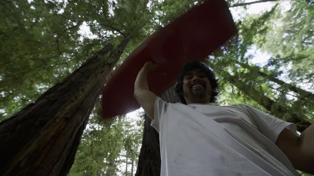 Smiling Man Lifting Red Board Above Head And Spinning It Within Redwoods