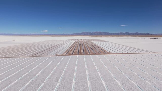 Drone aerial video of geometric salt evaporation rows across Salinas Grandes, Argentina under clear mountain sky.