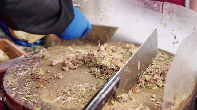 Two large cleavers lie on a wooden cutting board with chopped food ingredients for cooking preparation.