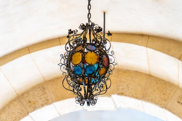 Ornate wrought-iron chandelier with colored glass hanging under a stone arch, Bojnice Castle © pszabo