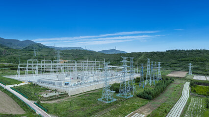 Fototapeta premium Modern Substation with Transmission Towers Amid Green Hills and Farmland