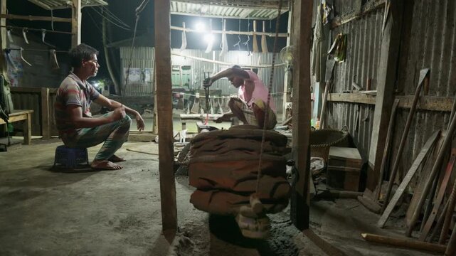 Traditional South Asian Bangladeshi blacksmith reshaping glowing red-hot metal sickles with hammer on anvil