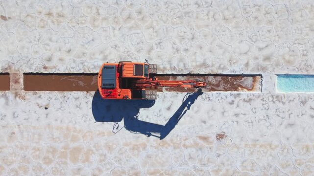 Drone aerial video directly above excavator digging salt extraction channel in Salinas Grandes, Argentina.