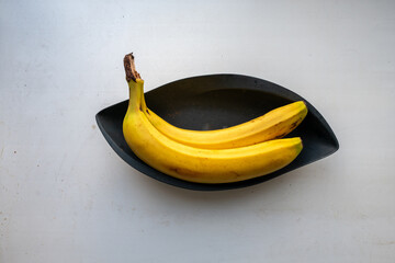 Two ripe bananas in a black decorative bowl on a white countertop — Overhead food still life. © Arkadii