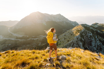 Obraz premium Female hiker with backpack on edge of a mountain feels free. Hiker enjoys the mountain scenery and walks along hiking trail in mountains. Concepts of hiking, adventure, and nature.