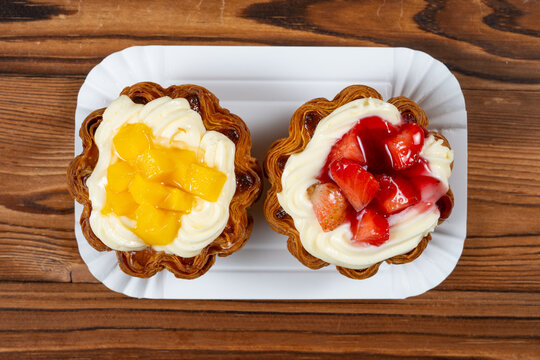 Two flaky layered fruit tarts filled with creamy custard, one topped with fresh mango cubes and the other glazed strawberry chunks