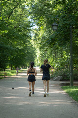 Fototapeta premium Two diverse fitness girlfriends running on path in public park. Active ladies training outdoor for healthy lifestyle. Group of women doing cardio workout exercise in nature on sunny summer day.