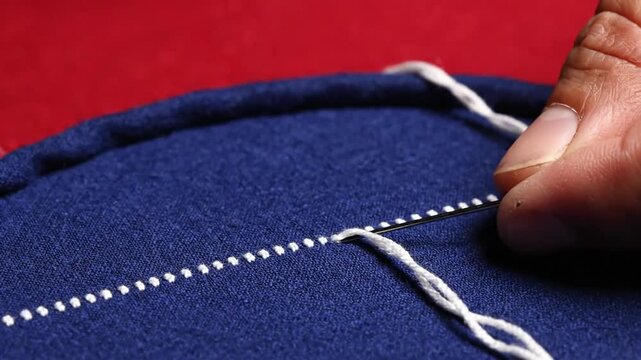 Close up of hands sewing white thread on blue fabric.