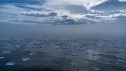 Eisschollen in der Hinlopenstraße, darüber Nebel und im Hintergrund schneebedeckter Berggipfel, pure Wildnis © Johannes