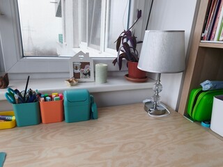 Children's workspace interior with an elegant desk lamp, book shelf and bright pencil holders on a wooden table, copy space © babanova