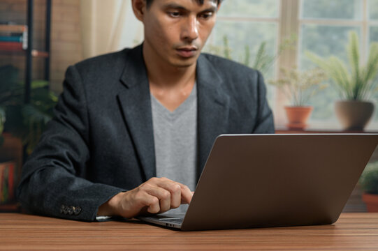 Young Man Working on Laptop at Modern Office Desk with Plants and Windows