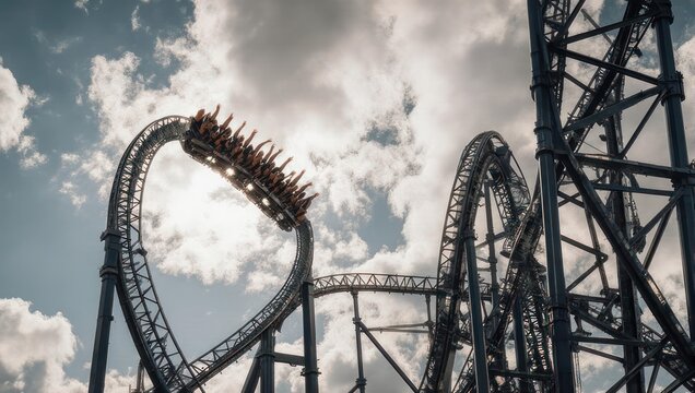Thrill ride crests a loop against a cloudy sky, passengers arms raised