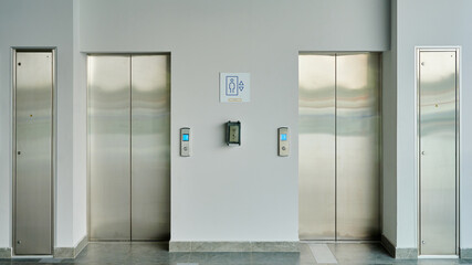 Two modern stainless steel elevator doors side by side in a clean building hallway © khmelev