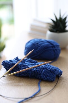Skein of pink yarn, sample and knitting needles on wooden cabinet indoors, closeup