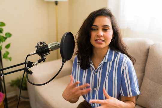 Cute woman recording engaging podcast episode in home studio, speaking into a professional microphone and gesturing expressively
